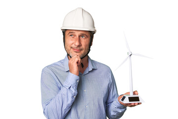 A middle-aged architect man holding a windmill model looking sideways with doubtful and skeptical expression.