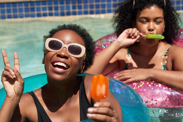 Two Black friends pose in the swimming pool eating ice lolly popsicle - Powered by Adobe