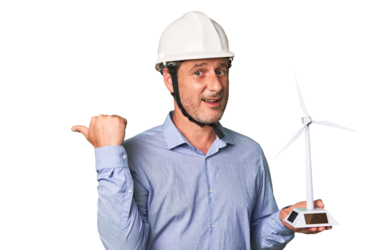 A middle-aged architect man holding a windmill model points with thumb finger away, laughing and carefree.