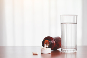 A glass of drinking water with piles of tablets were released from the brown bottle