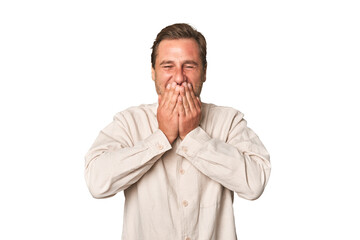 A middle-aged man isolated laughing about something, covering mouth with hands.