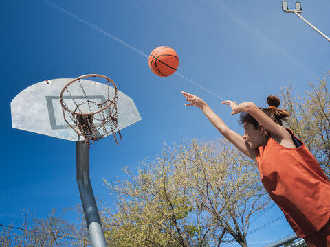 Basket shot by a boy with long hair in a bun on an outdoor court.