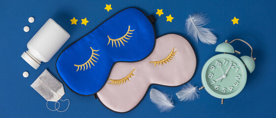 Blue and pink sleeping masks, pills, alarm clock and herbal tea on blue background, concept of...