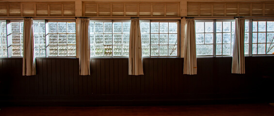 Interior de casa antiga de madeira com diversas janelas quadradas com cortina. Ambiente escuro e...