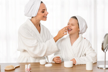 Obraz na płótnie Canvas Loving mother applying skincare cream on face of happy little daughter