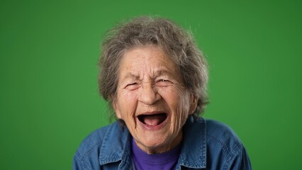 Funny crazy closeup portrait of happy laughing elderly senior old woman with wrinkled skin and grey hair on green screen background.