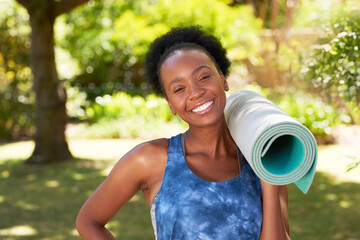 Portrait of a Black woman standing ready for yoga in park, rolled up mat