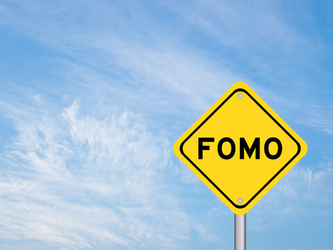 Yellow transportation sign with word FOMO (abbreviation of fear of missing out) on blue color sky background