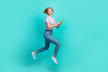 Fototapeta na wymiar Full length photo of charming positive girl stylish t-shirt denim pants hold smartphone running isolated on turquoise color background