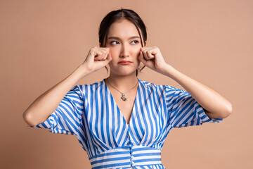 asia woman hand gesture pretend crying fashion photo shoot,sadness asian female woman look at camera hand clean tear drop from her eye studio shot on brown colour background - obrazy, fototapety, plakaty