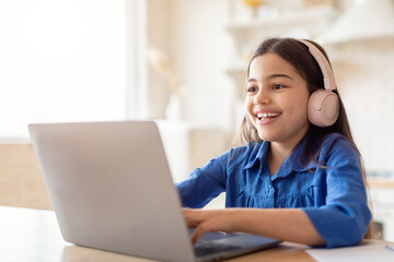 Happy Schoolgirl Studying Online Using Laptop Wearing Headphones At Home