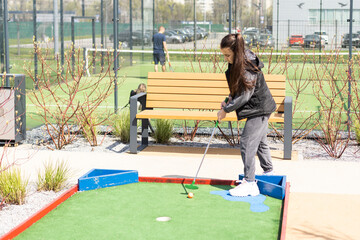 Beautiful toddler european model child girl posing with mini golf equipment on green field outdoor in tropical resort.
