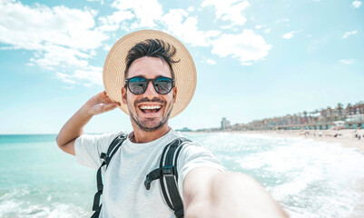 Happy man with hat and sunglasses taking selfie picture with smartphone at the beach 