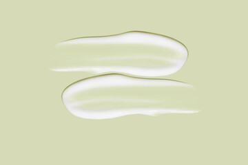 Lots of smears of cosmetic cream. Light, smooth surface.  In a row. At an angle. Top view. Texture of flowing cream. Liquid creamy strokes. On green background. Cosmetic background, banner.