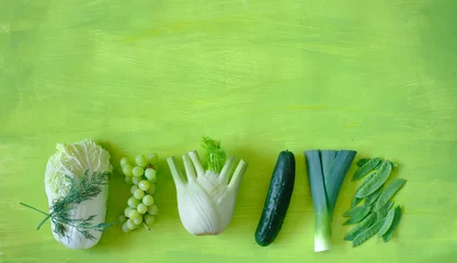 Fotobehang healthy food, celery cabbage, grapes, fennel, cucumber, snow pea, leek, free copy space, on green background, concept, flat lay, © Kirsten Hinte