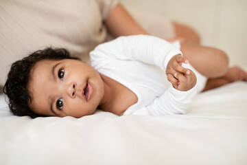 Obraz na płótnie Canvas Smiling cute curly african american little child in soft clothes lie on white bed, relax, sleep time in bedroom interior