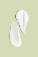 Lots of smears of cosmetic cream. Light, smooth surface.  In a row. At an angle. Top view. Texture of flowing cream. Liquid creamy strokes. On green background. Cosmetic background, banner.