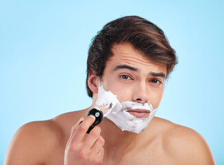 The smoother the face the smoother the man. Shot of a young man shaving his face against a studio...