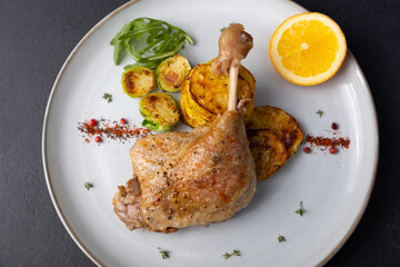Duck leg confit with Brussels sprouts, baked potatoes, thyme and orange. Traditional French cuisine. Selective focus, close-up, black background.