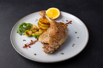 Duck leg confit with Brussels sprouts, baked potatoes, thyme and orange. Traditional French cuisine. Selective focus, close-up, black background.