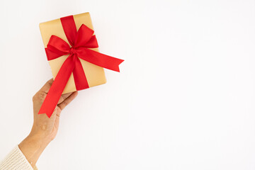 close up woman hands in white sweater giving  Christmas holiday golden gift  box with red ribbon. - copy space