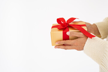 close up woman hands in white sweater giving  Christmas holiday golden gift  box with red ribbon. - copy space