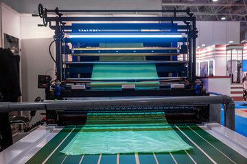 Cutting bag making machine with flat polyethylene green film at exhibition, trade show. Manufacturing, recycling, industry and automated technology equipment concept
