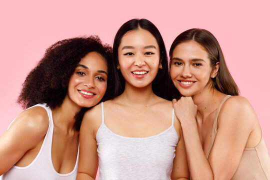 Diversity and beauty concept. Portrait of happy three multiethnic ladies posing and smiling to camera, pink background