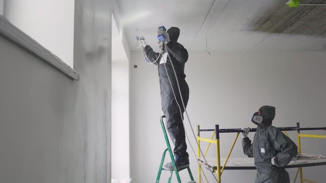 Wall spray painting. Two builders painters paint the walls in the room with a special paint sprayer