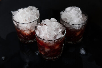 Alcoholic cocktail with ice closeup in old fashion glasses on a black concrete background