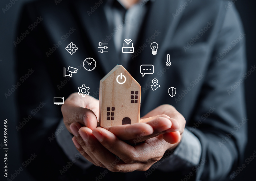Poster Smart home digital remote control on smartphone concept. internet of things in technology control. Businessman holding wooden house with virtual smart home icon function.