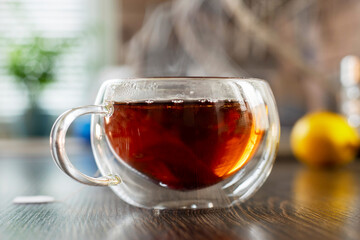 A hot cup of freshly brewed black tea with steam on wooden table