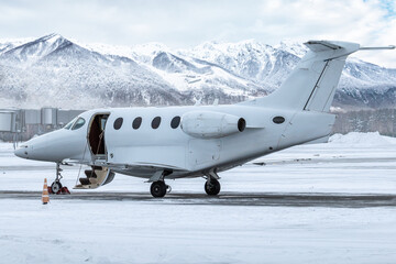 Modern white private jet with an opened gangway door at the winter airport apron on the background...