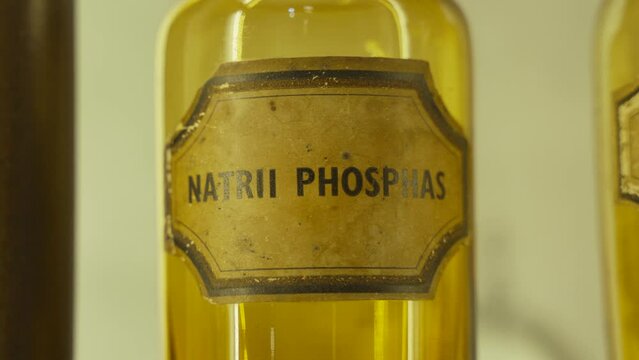 Glass old brown jar of Sodium phosphate on shelf in cupboard with warm light, close-up. Worn sticker with inscription in Latin on container with drug to maintain mineral balance in body.