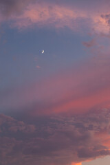 The orange pink sunset sky with a quarter moon. The quarter moon is visible in the blue sky. The clouds are pink to orange-grey.