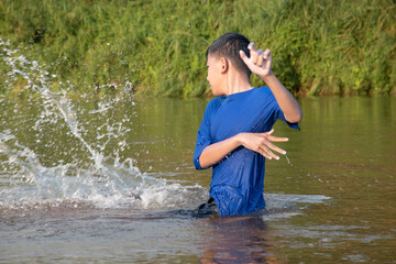 Asian boy in blue t-shirt is spending his freetimes by diving, swimming, throwing rocks and catching fish in the river happily, hobby and happiness of children concept, in motion.