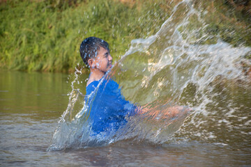 Asian boy in blue t-shirt is spending his freetimes by diving, swimming, throwing rocks and catching fish in the river happily, hobby and happiness of children concept, in motion.