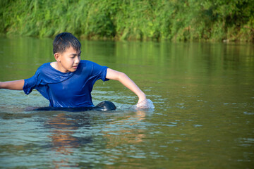 Asian boy in blue t-shirt is spending his freetimes by diving, swimming, throwing rocks and catching fish in the river happily, hobby and happiness of children concept, in motion.