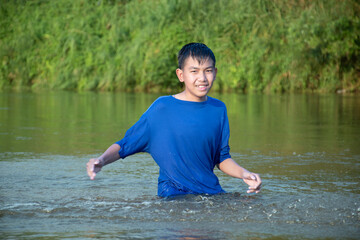 Asian boy in blue t-shirt is spending his freetimes by diving, swimming, throwing rocks and catching fish in the river happily, hobby and happiness of children concept, in motion.