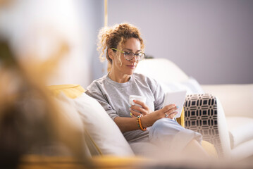 Modern lady having relax at home sitting on couch and using ereader tablet to read an online ebook....