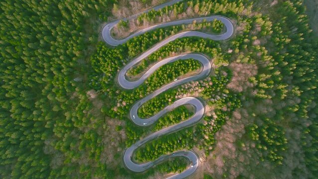 Aerial view of a winding road in the mountains shoot from a drone while lowering altitude. The video was shoot with the camera tilted downwards for a top view of the serpentines and the traffic.