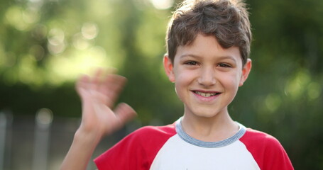 Handsome young boy child waving to camera with hand smiling outdoors © Marco
