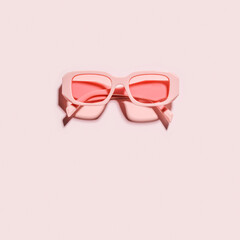 Minimal pink eyeglasses with rose tinted color glasses on pink background, pastel monochrome card, summer romance concept. Top view aesthetic plastic-framed sunglasses, minimal flat lay