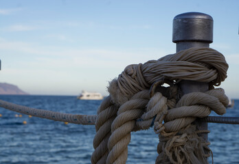 Fototapeta premium The corner of a boat dock, on a lake, with rope wrapped around pilings. Mooring rope and bollard on sea water and yachts background. Shot with copy space.