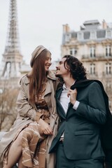 A couple in love walks along the streets of Paris, a guy in a coat and a suit, a girl in a dress with a beret and a trench coat in autumn