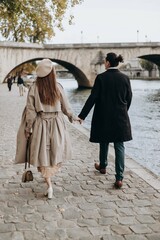 A couple in love walks along the streets of Paris, a guy in a coat and a suit, a girl in a dress with a beret and a trench coat in autumn