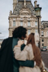 Fototapeta na wymiar A couple in love walks along the streets of Paris, a guy in a coat and a suit, a girl in a dress with a beret and a trench coat in autumn soft focus
