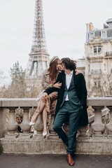A couple in love walks along the streets of Paris, a guy in a coat and a suit, a girl in a dress with a beret and a trench coat in autumn