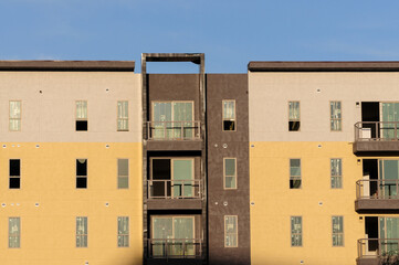 Exterior view of top floors of a new apartment building with walls painted in yellow, beige and brown colors showing sliding doors, balconies and windows