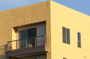 Detail of an exterior corner of the top floor of a new apartment building painted in yellow color showing a balcony, a sliding glass door, and windows